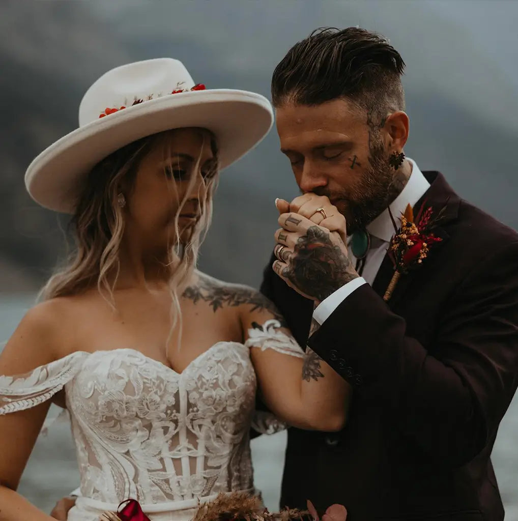 modern bride and groom holding hands while the groom kisses her hand. Both are wearing wedding bands.